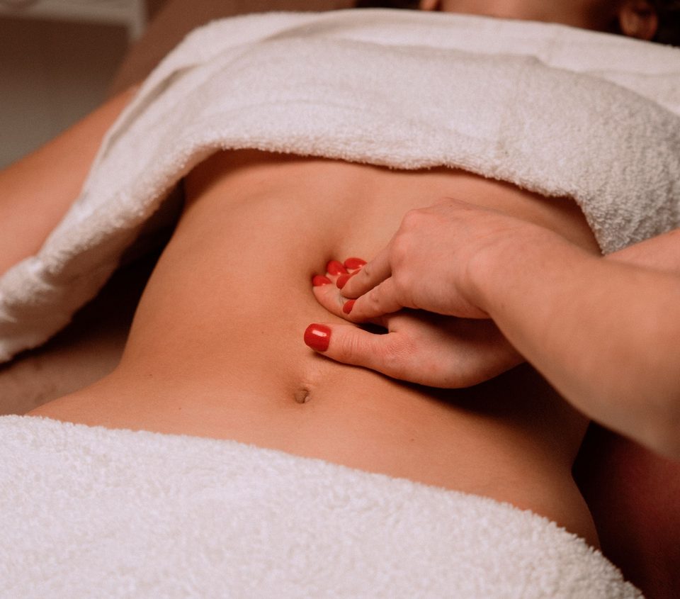 Hands gently massaging a person&rsquo;s abdomen, draped with a towel