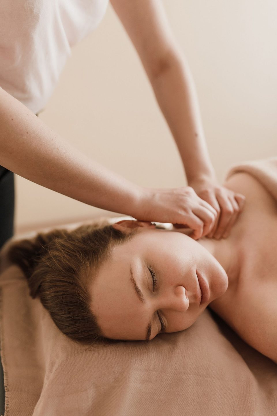 A woman rests face up with her eyes closed as a therapist&rsquo;s hands massage her neck and shoulder