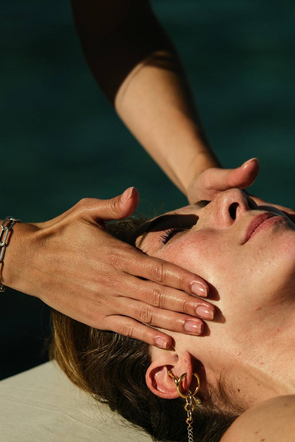 Hands massaging a person&rsquo;s face and jaw in warm sunlight