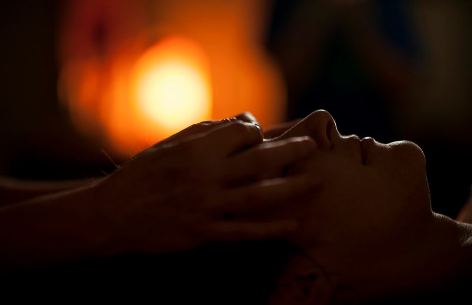 Hands gently massaging a person&rsquo;s face in a softly lit room