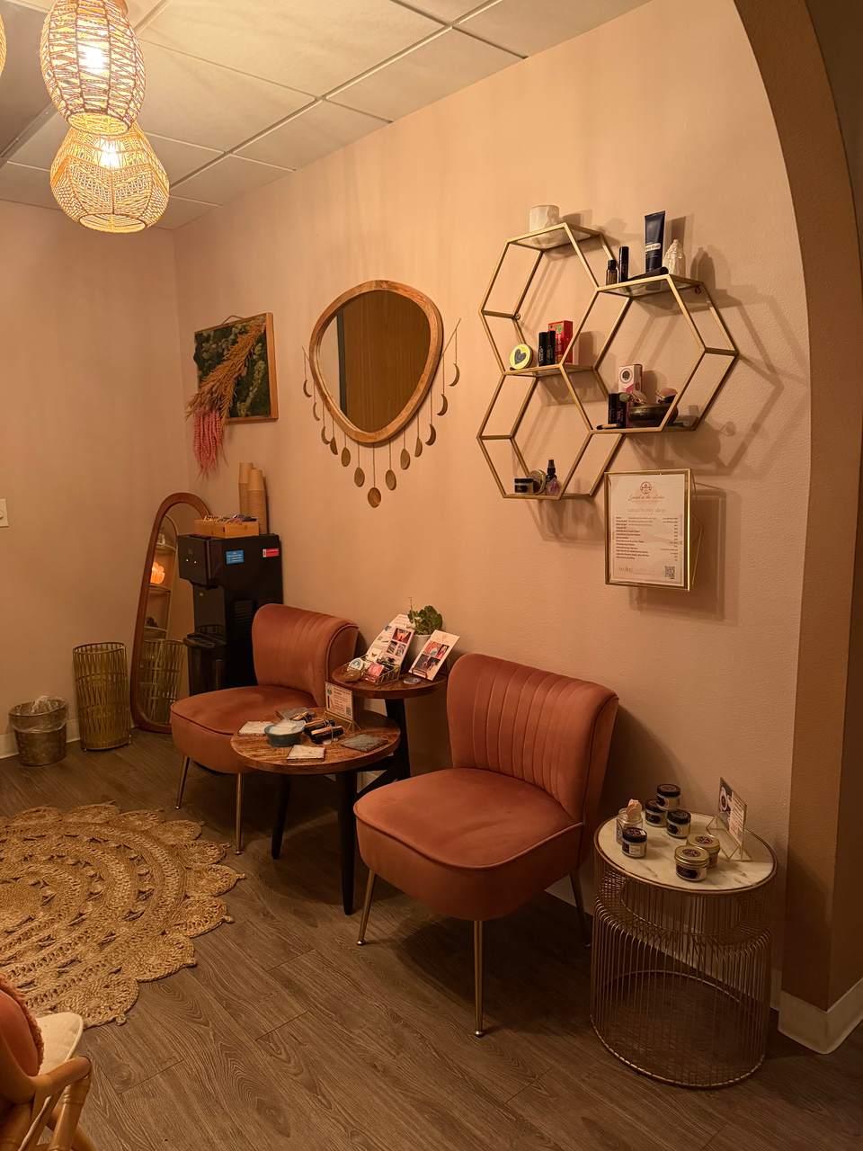 Waiting area with terracotta velvet chairs, a gold moon-phase mirror, and woven pendant lights