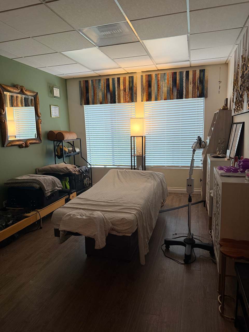 Treatment room with a massage table, soft lamp light, and a sage green wall