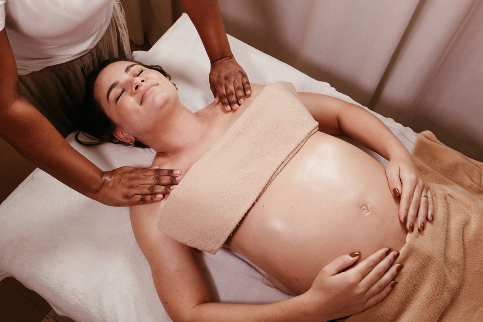 A pregnant woman lying back comfortably while a therapist massages her shoulders
